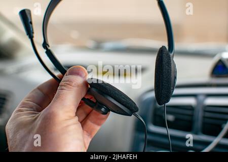 view of stereo headphones with soft foam pads with a microphone in the hand of a person, a driver inside a car Stock Photo