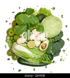 Bunch of greens and herbs laid on white countertop. Halved avocado, lettuce salad leaves, raw broccoli and other vegetables in row. Vegan diet concept Stock Photo