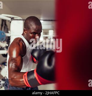 Sweaty young boxer working out with a red punching bag at the gym ...