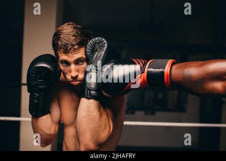 Boxing athlete blocking a punch to his jaw during a match with his opponent. Two male boxers fighting in a boxing ring. Stock Photo