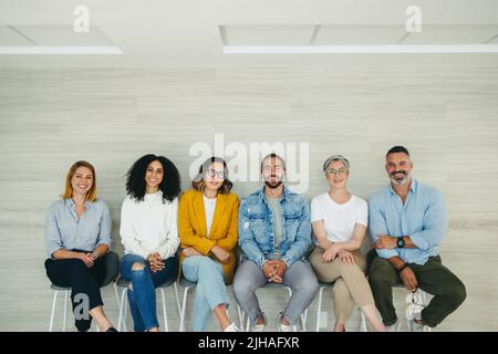 Happy job applicants smiling at the camera while sitting in line for an interview. Group of multicultural businesspeople waiting for an opportunity fo Stock Photo