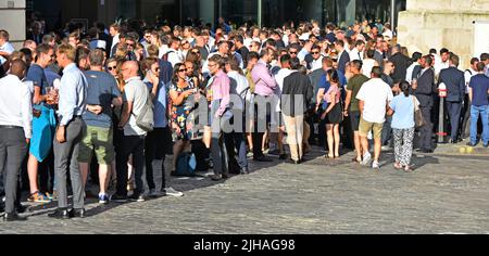 Office workers overflowing out of pub interior to socialise onto pavement & cobbled road some drinking alcohol standing in evening sunshine London UK Stock Photo