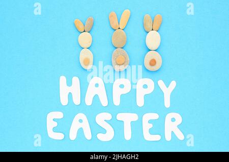 Happy Easter lettering and bunnies from pebbles on blue background. Flatlay postcard creative concept. Creative greetings with natural craft materials Stock Photo