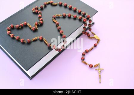 Rosary wooden beads and crucifix christian cross on holy bible book on violet background. Catholic symbol. Flatlay, top view. Pray and faith for God Stock Photo