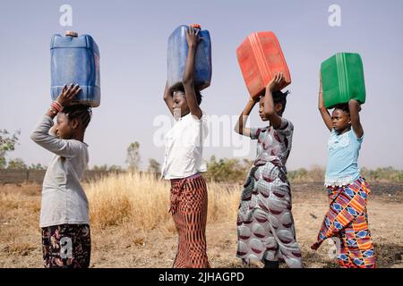 Four very young African girls marching in a line with colored canisters on their heads, sympolising that fetching water is a woman's job, regardless o Stock Photo