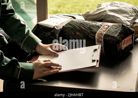 A young man writing on a blank paper with clipboard and with stack of delivery parcels as background Stock Photo