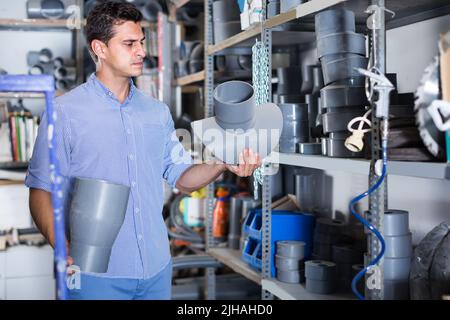concentrated male is choosing plastic trumpet in the plumbing department in store Stock Photo