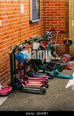 Children's scooters of different colours parked outside a school in Canterbury, UK Stock Photo