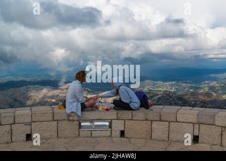 Young couple having lunch on the edge of the Guvno lookout point of the Mausoleum og Njegos. Montenegro Stock Photo
