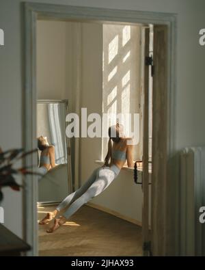 Fitness, yoga, stretching and healthy lifestyle concept - young woman doing exercises near window at home Stock Photo