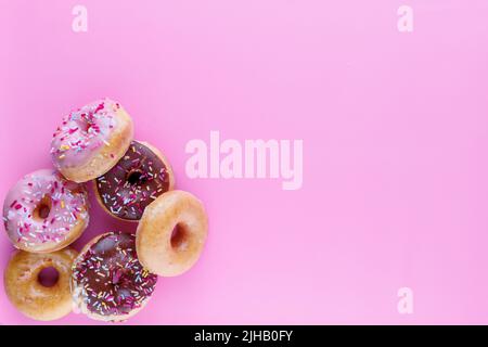Sugar icing glazed doughnuts, including a chocolate sprinkle-topped variety, arranged in a flat lay on a solid background with negative space. Stock Photo