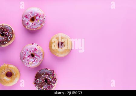 Sugar icing glazed doughnuts, including a chocolate sprinkle-topped variety, arranged in a flat lay on a solid background with negative space. Stock Photo