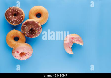 Sugar icing glazed doughnuts, including a chocolate sprinkle-topped variety, arranged in a flat lay on a solid background with negative space. Stock Photo