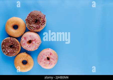 Sugar icing glazed doughnuts, including a chocolate sprinkle-topped variety, arranged in a flat lay on a solid background with negative space. Stock Photo