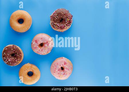 Sugar icing glazed doughnuts, including a chocolate sprinkle-topped variety, arranged in a flat lay on a solid background with negative space. Stock Photo