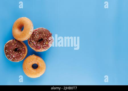Sugar icing glazed doughnuts, including a chocolate sprinkle-topped variety, arranged in a flat lay on a solid background with negative space. Stock Photo