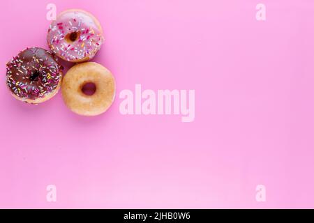 Sugar icing glazed doughnuts, including a chocolate sprinkle-topped variety, arranged in a flat lay on a solid background with negative space. Stock Photo