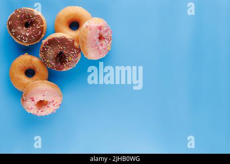 Sugar icing glazed doughnuts, including a chocolate sprinkle-topped variety, arranged in a flat lay on a solid background with negative space. Stock Photo