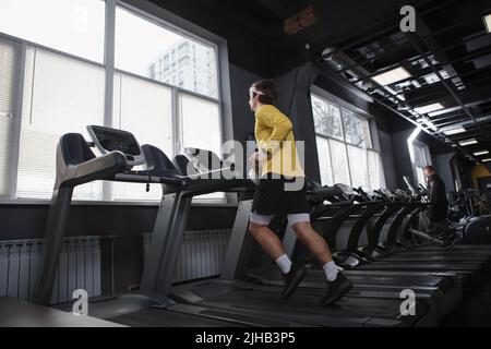 Full length shot of a man doing cardio workout at gym, running on treadmill Stock Photo