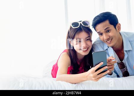 Happy Asian couple holds mobile phone. Young man and woman in casual feel happy with smiling and excited while having and looking at smartphone screen Stock Photo