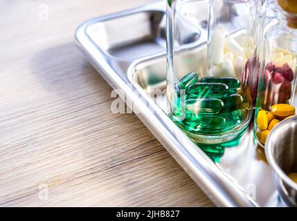 Close up vitamins and supplements in the small clear glass bottles in the steel medical tray on wooden table with copy space. Green, yellow, red, whit Stock Photo