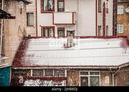 Smoke rises from the chimney on the house. Roof with smoking chimney in snowing winter Stock Photo