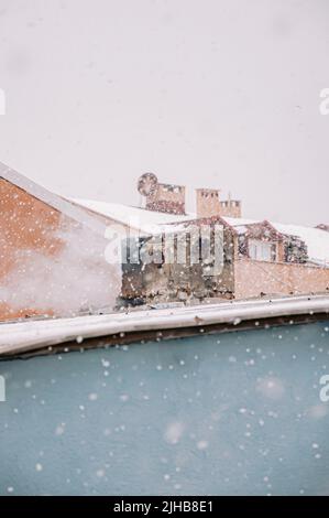 Smoke rises from the chimney on the house. Roof with smoking chimney in snowing winter Stock Photo