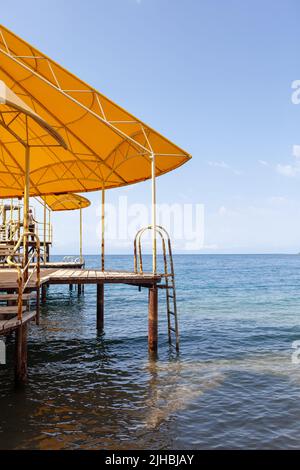 Swimming area or pier on the sea. A large pier with a roof, wooden planks and rusty stairs descending into the water. Bathing and resting place. Stock Photo