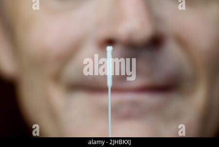 Covid-19 test, nose swab with male face in the background. Stock Photo