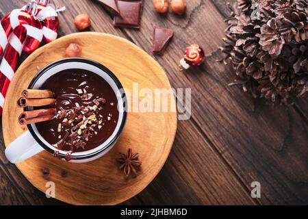 Hot chocolate. Homemade spicy hot chocolate with cinnamon, crushed hazelnut in enamel mug on  old wooden background. Cozy seasonal holidays. Stock Photo