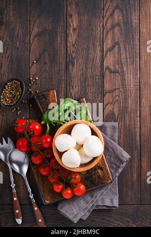 Caprese salad, ingredients for cooking. Cutting wooden board with traditional  caprese preparation ingridients: mozzarella, tomatoes , basil, olive oi Stock Photo