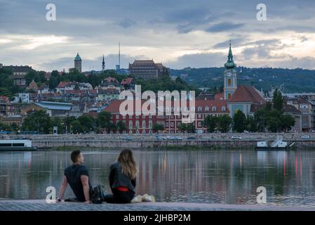 Unfocused relaxed couple sitting by the river against old city in dusk Stock Photo