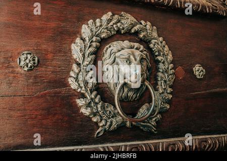 Decorative door carved knocker - head of lion in old style. Handle with ring in mouth. Ancient metal on czech building. Stock Photo