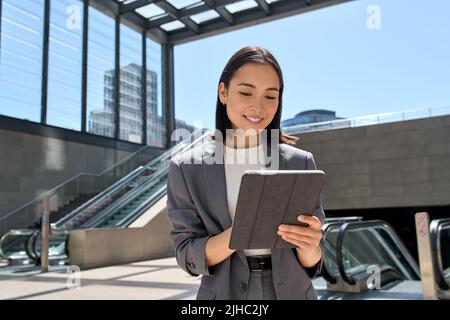 Smiling Asian young business woman standing in city subway using tablet. Stock Photo