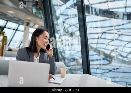 Young happy Asian business woman wearing suit talking on phone in office. Stock Photo