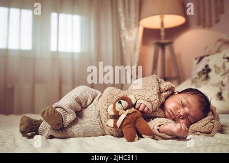 Infant multiethnic baby boy sleeping on a bed. Looking cozy with teddy bear Stock Photo