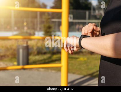 Woman using fitness tracker for steps number or heart rate monitoring during exercise at stadium. Physical activity tracking by means of electronic device. High quality photo Stock Photo