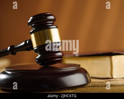 Close-up. Judge's wooden gavel and an open book in the background. Beige background. Court, crime, lawyer, judge, rule of law, constitution, legality. Stock Photo