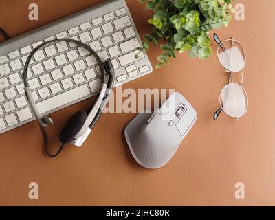 On the desktop, a personal computer keyboard, headphones, a mouse, glasses and an indoor flower on a beige background. Low angle view. Comfortable pla Stock Photo