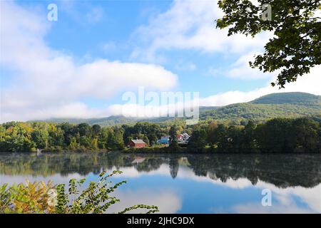 Vermont lake with beautiful farm nestled in the woods and fall colors starting to emerge as a light mist accentuates the beauty of this place Stock Photo