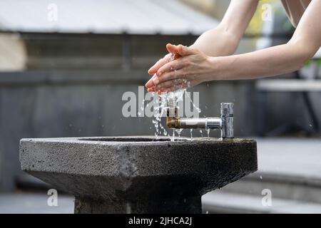 Hands with water pouring from tap in street. Drops of water streaming up on fingers of young girl.  Stock Photo