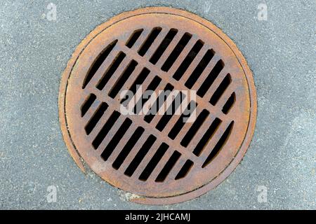 Looking directly down at a round storm sewer set in asphalt. The metal is covered with light surface rust. Stock Photo