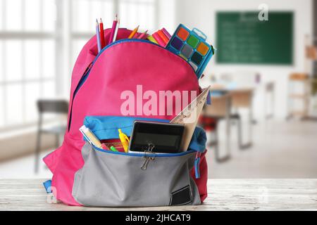 School backpack with stationery on table in classroom Stock Photo