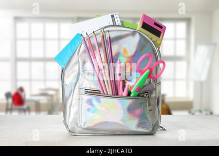 School backpack with stationery on table in classroom Stock Photo