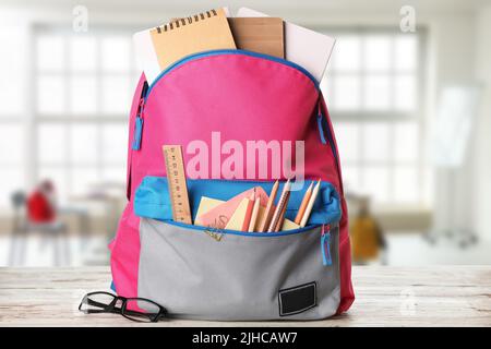 School backpack with stationery on table in classroom Stock Photo