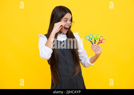 Teenage school girl with scissors, isolated on yellow background. Child creativity, arts and crafts, diy tools. Stock Photo