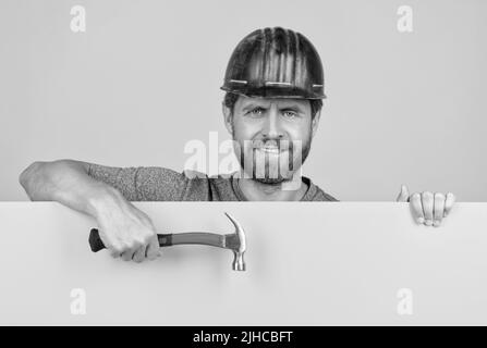 happy mature man laborer in helmet behind yellow paper for copy space hold hammer, happy workers day Stock Photo