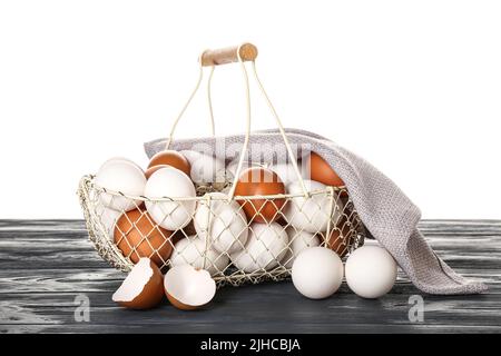 Basket with different chicken eggs on dark wooden table against white background Stock Photo