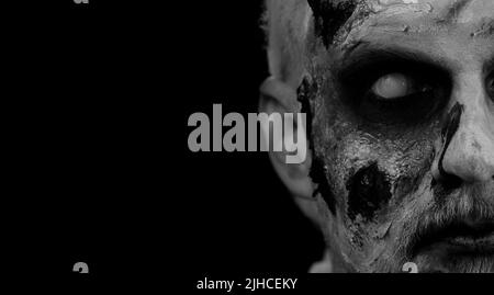 Close-up face of sinister man with horrible scary Halloween zombie makeup making faces, looking ominous at camera, trying to scare. Dead guy with wounded bloody scars face isolated on black background Stock Photo