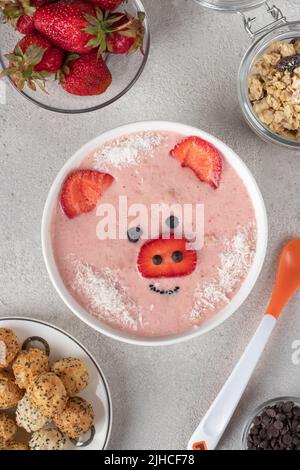 Fun food for kids - smoothie-bowl in shape funny piglet, with strawberries, granola, chocolate and crispy balls, Top view on gray background Stock Photo